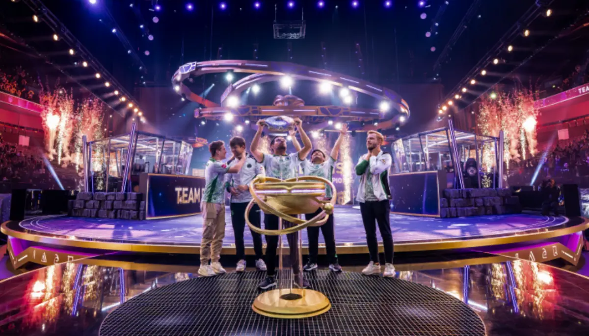 Fem esportspelare firar seger på scen med pokal och konfetti under en stor turnering i en arena.