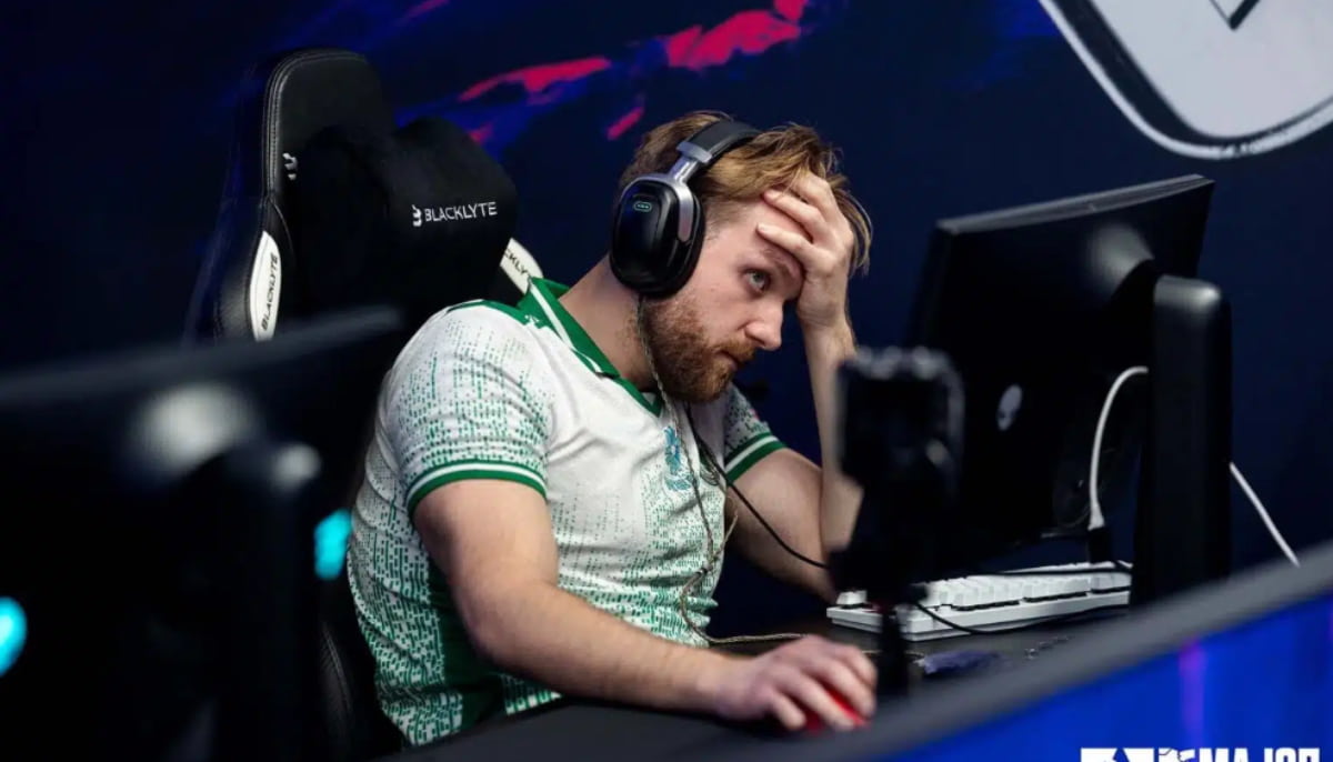 E-sportspelare i grönvit tröja sitter vid dator, håller handen för ansiktet och verkar frustrerad.